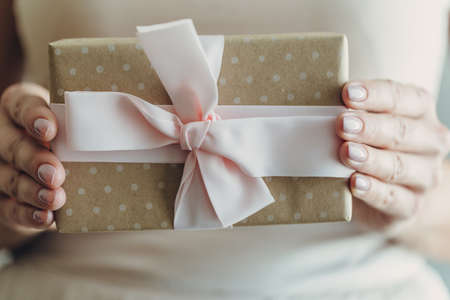 Close-up of female hands holding a small gift wrapped with a satin ribbon. A small gift in the hands...