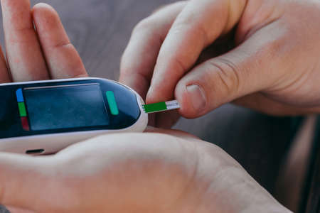 medicine, diabetes, medicine and people concept - close up of a man with a blood glucose meter and a test strip checking blood sugar at home. Diabetes Day, November 14の写真素材