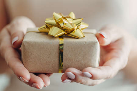 Close-up of female hands holding a small gift wrapped with a satin ribbon. A small gift in the hands of a woman indoors.の写真素材