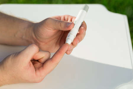 Man taking a blood sample with a lancet handle outside against the backdrop of greenery. Diabetes,...