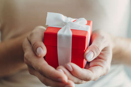 Close-up of female hands holding a small gift wrapped with a satin ribbon. A small gift in the hands...