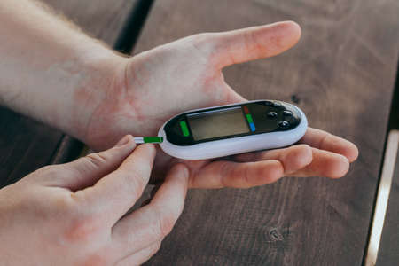 medicine, diabetes, medicine and people concept - close up of a man with a blood glucose meter and a...