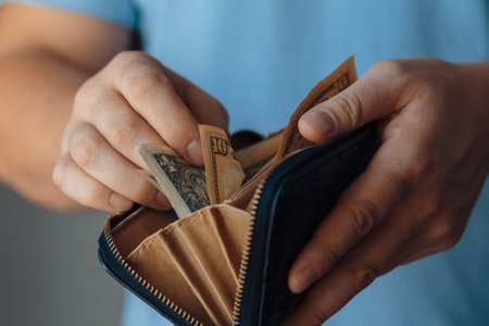 wallet with tiny paper dollar bills in a wallet in the hands of a bankrupt man. Reducing the cost of...
