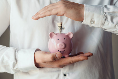 a man's hands in a white shirt puts a one dollar bills in a pink piggy bank. Accumulation concept, insuranceの写真素材