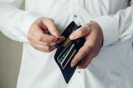 wallet in the hands of a bankrupt man. hand puts one coin. Poverty concept, crisis. dismissal or cost savingsの写真素材