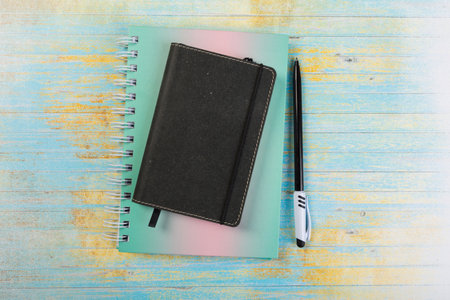 stack of school exercise books and spiral notepads with ballpoint pen on blue wooden background