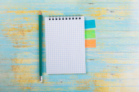 stack of school exercise books and spiral notepads with ballpoint pen on blue wooden background