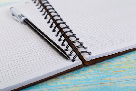 stack of school exercise books and spiral notepads with ballpoint pen on blue wooden background