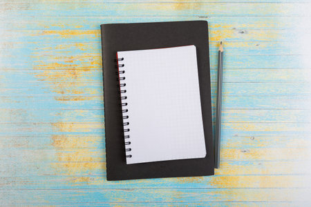 stack of school exercise books and spiral notepads with ballpoint pen on blue wooden background