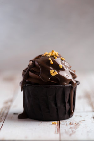 brown cream muffins poured with chocolate and sprinkled with nuts on a light wood. delicious dessert, close-upの写真素材