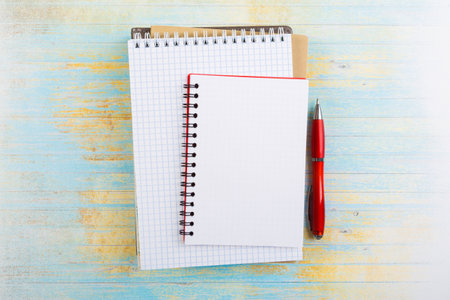 stack of school exercise books and spiral notepads with ballpoint pen on blue wooden background....