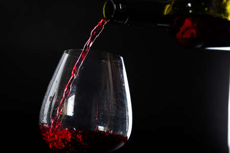 Pouring red wine into a glass on a black background. splashes and dropsの写真素材