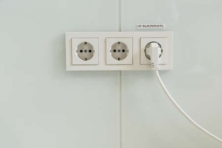 several plastic socket, white, mounted on a gray wall. one outlet in use, power cord included