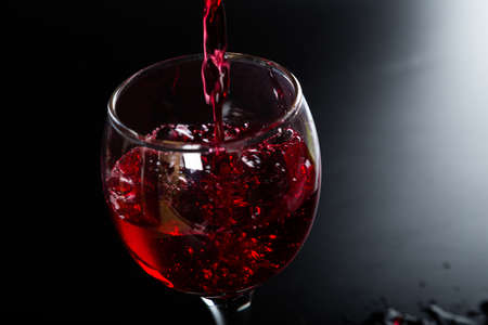 Pouring red wine into a glass on a black background. splashes and drops