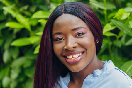 close-up portrait of smiling young African American girl with pink hair outdoors on a sunny day.の写真素材