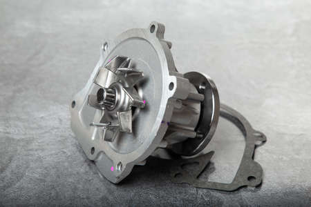 new car water pump with gasket and timing belt on gray table.