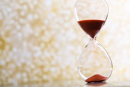 Sand passes through an hourglass, measuring the travel time in a countdown against a golden bokeh...