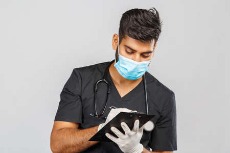 cute indian doctor or surgeon in black uniform with stethoscope and white latex gloves, blue medical mask on gray backgroundの写真素材