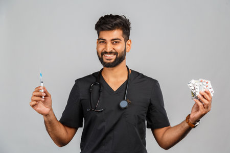 indian doctor or surgeon in black uniform with stethoscope, syringe and pills on gray backgroundの写真素材