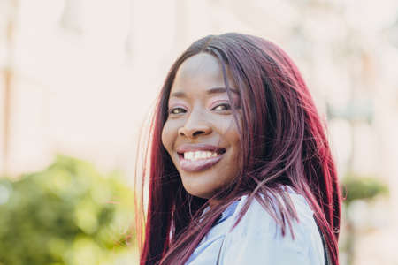 Portrait of a smiling young African American girl with pink hair and a blue shirt walking outside on a sunny day.の写真素材