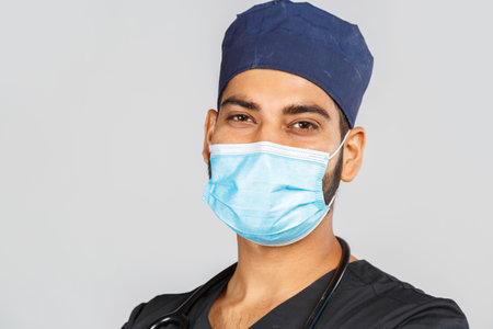 cute indian doctor or surgeon in black uniform with stethoscope and white latex gloves, blue medical mask on gray backgroundの写真素材