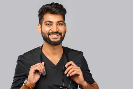 amusing young indian doctor or surgeon with stethoscope on gray backgroundの写真素材