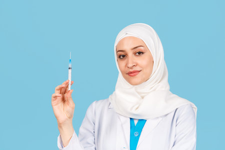 Portrait of a friendly, Muslim doctor or nurse woman with stethoscope and syringe in her hand in a white coat. on a blue background. medicine and healthcareの写真素材