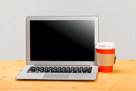 Laptop with blank screen for product display and cup of coffee on wooden tableの写真素材