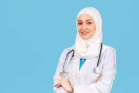 Portrait of a friendly, Muslim doctor or nurse woman in hijab with a stethoscope in a white coat. on a blue background. medicine and healthcareの写真素材