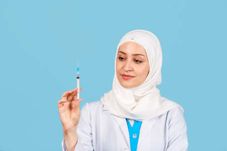 Portrait of a friendly, Muslim doctor or nurse woman with stethoscope and syringe in her hand in a white coat. on a blue background. medicine and healthcareの写真素材