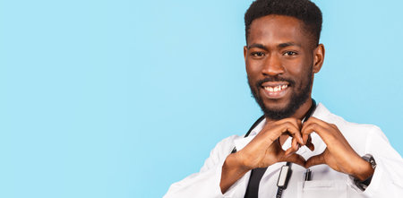 African American male doctor with stethoscope in white coat shows heart sign with hands on blue background. medicine, profession and healthcare concept.の写真素材