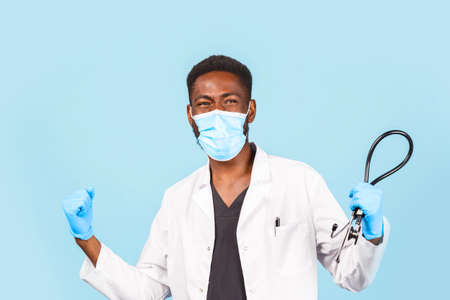 joyful African American male doctor with stethoscope wearing mask and gloves on blue background....