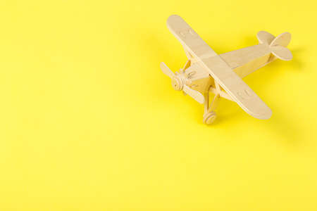 Model of a wooden toy plane, airliner, on a yellow background. travel and tourism concept, air...