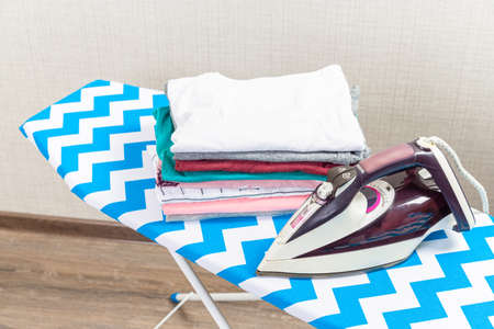 Folded ironed men's shirts lie next to the iron on the ironing board.