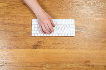 Office worker checks email while sitting at a wooden table.の写真素材