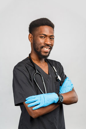 happy young african or afro american doctor or surgeon with stethoscope and blue gloves standing against gray backgroundの写真素材