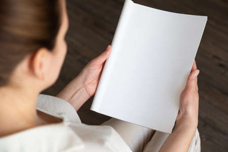 beautiful female hands holding white magazine with blank cover mock up at homeの写真素材