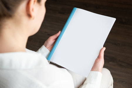 beautiful female hands holding white magazine with blank cover mock up at homeの写真素材