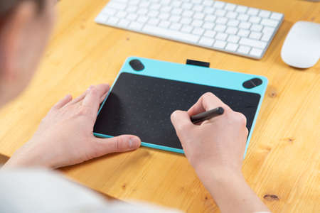 Close-up of female hands using digital graphics tablet and stylus while working in modern officeの写真素材
