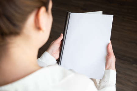 Woman holding brochure with blank cover on wooden background, top view. Mock up for designの写真素材