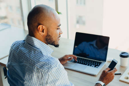 Have a nice working day. Confident young african american businessman working on laptop and talking...