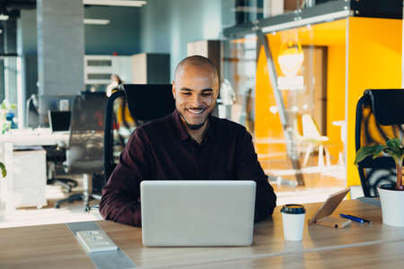 Have a nice working day. Confident young african american businessman working on laptop and talking...