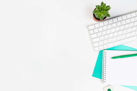 White office desk with blank laptop, computer keyboard and other stationery, potted plant.の写真素材