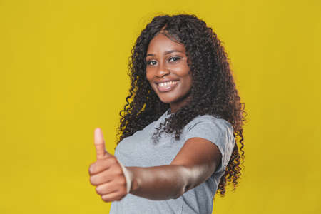 Beautiful african american girl with afro hairstyle smiling and showing thumbs up with her hands on yellow backgroundの写真素材