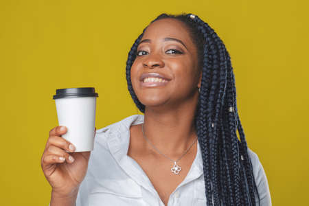 beautiful african american girl with takeaway coffee cup in hands on yellow backgroundの写真素材