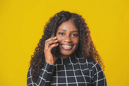 beautiful african american girl uses her mobile phone to chat happily smiling on yellow background