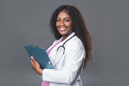 Young nurse using a clipboard against a gray background. Portrait Of Female Nurse with a stethoscope in pink uniformの写真素材