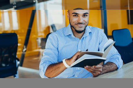 Handsome cheerful african american man in creative atmosphere using laptop sitting on a wooden table.の写真素材