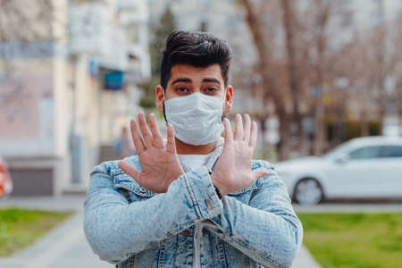 Fashionably dressed young Indian man in a medical mask walks on the street. hygienic mask to prevent infection, airborne respiratory illness.の写真素材