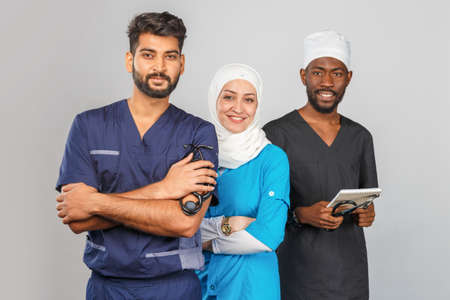 Group of paramedics smiling over gray background. muslim doctor woman with colleagues african and indian surgeonの写真素材